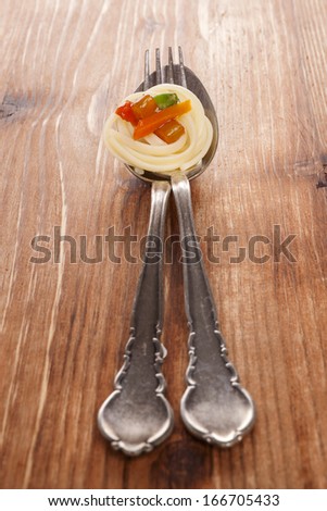 Culinary pasta eating. Pasta with colorful vegetable on silver spoon with fork isolated on brown wooden background.