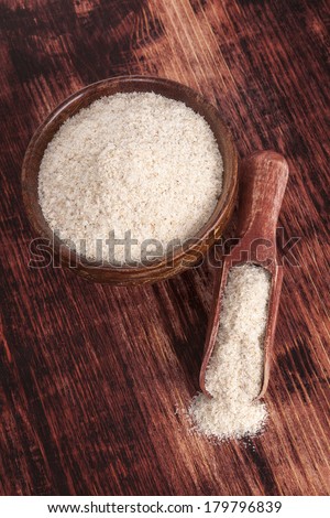 Dietary fiber psyllium in round wooden bowl on dark brown wooden background, top view. Healthy eating concept.