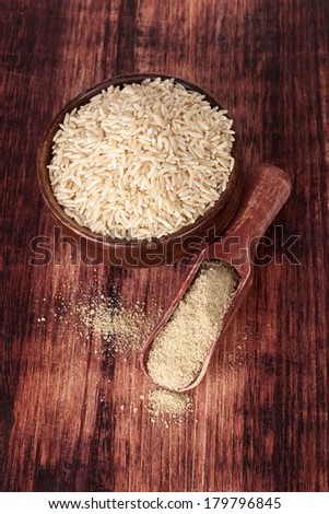 Rice in round wooden bowl with dietary rice fiber on wooden spoon on dark brown wooden background, top view. Healthy eating concept.