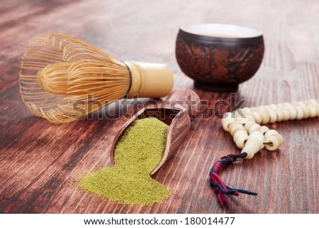 Traditional tea ceremony. Powdered green tea matcha, hot tea in ceramic cup, bamboo chasen and buddhist necklace on brown wooden background.