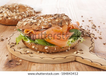 Salmon whole grain bagel on wooden kitchen board on wooden background. Traditional bagel eating.