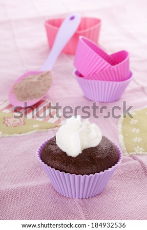 Modern contemporary baking background in purple and pink. Chocolate cupcake and baking forms with whipped cream on pink background.