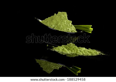 Green powder in bowl and grass blades isolated on black background. Healthy nutritional supplements. Green superfood, detox concept.