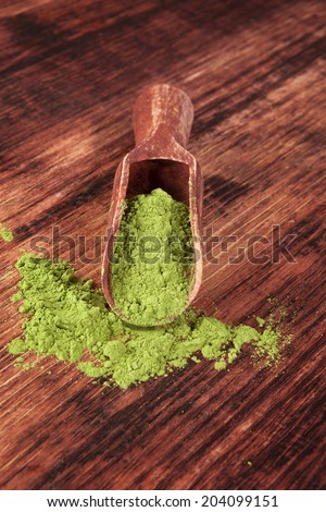 Green food supplement. Wheatgrass ground on brown wooden scoop on brown wooden background. Healthy natural detox.