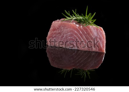 Tuna steak isolated on black background. Raw fresh tuna steak with rosemary herbs on black. Culinary tuna steak eating.