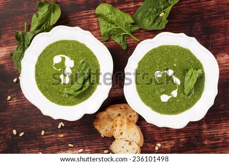 Delicious fresh spinach soup with fresh spinach leaves and bread in two vintage plates on wooden background, top view. Culinary soup eating.