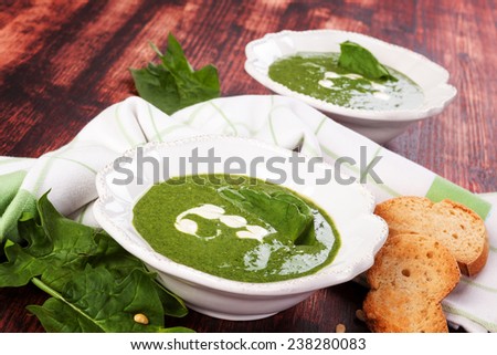 Spinach soup with spinach leaves and fresh bread on brown wooden background. Culinary spinach soup eating.