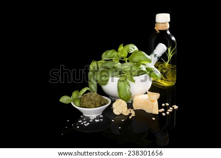 Basil pesto, fresh basil leaves, garlic, pamrmigiano cheese, olive oil and pine seeds isolated on black background. Mediterranean eating still life.