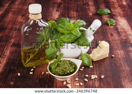 Basil pesto, fresh basil leaves, garlic, pamrmigiano cheese, olive oil and pine seeds on wooden background. Green pesto still life, country style.