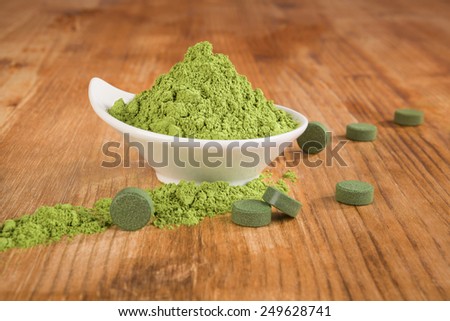 Detox. Chlorella pills and wheat grass powder in bowl on brown wooden background. Natural alternative medicine, weight loss and detox.
