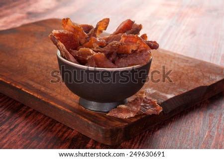 Beef jerky. Dried meat beef jerky on wooden chopping board on wooden background. Dry meat, rustic country style. Delicious meat eating.