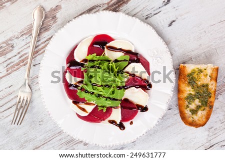 Beet with goat cheese and fresh salad on white vintage plate on white wooden textured background, top view. Culinary delicious healthy eating.
