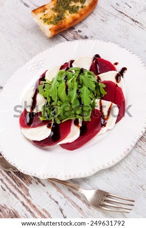 Beet with goat cheese and fresh salad on white vintage plate on white wooden textured background. Culinary delicious healthy eating.