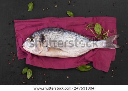 Delicious fresh sea bream fish on colorful napkin with colorful peppercorns on black textured stone table. Culinary healthy cooking.