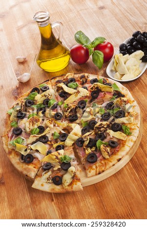 Delicious pizza background. Fresh pizza, garlic, olive oil, fresh herbs, tomatoes, artichokes and black olives on wooden background.
