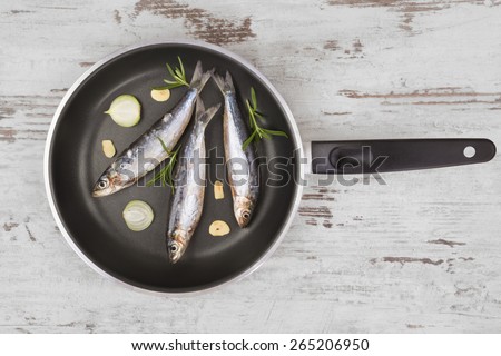 Fresh anchovy fish on black pan on white textured wooden background. Culinary seafood eating, mediterranean style.