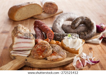 Blood sausage, rice sausage, head cheese, garlic, onion beer and bread on wooden kitchen board on wooden background. Traditional pork meat eating.