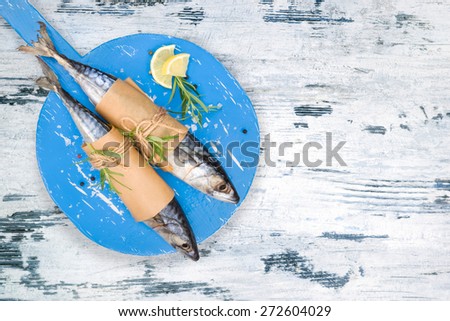 Delicious fresh mackerel fish on wooden kitchen board with fresh herbs and lemon on white and blue textured wooden background. Culinary healthy cooking.