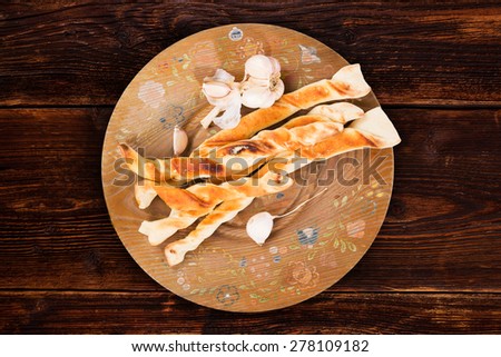 Pizza bread with garlic on wooden plate on brown vintage wooden table, top view. Culinary pizzastick eating, rustic styles.