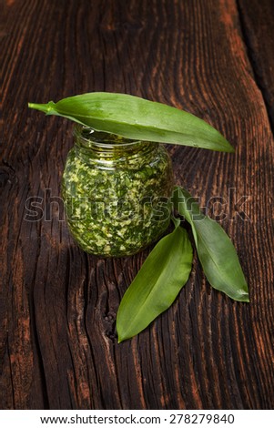 Garlic pesto with fresh wild garlic leaves on brown wooden textured background. Culinary healthy eating.