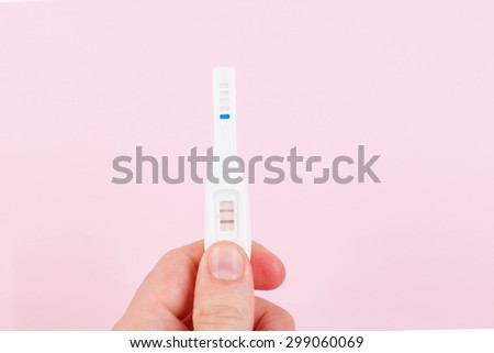 Male hand holding positive pregnancy test isolated on pink background. Happy father.