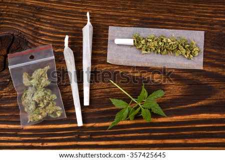 Marijuana background. Cannabis joint, bud in plastic bag and hemp leaves on wooden table. Addictive drug or alternative medicine.