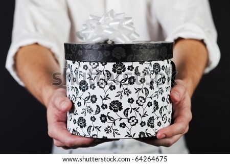 Male adult holding a round black and white decorated gift box with ribbon.
