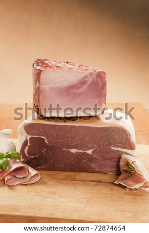 Prosciutto and ham piece with slices on wooden board.