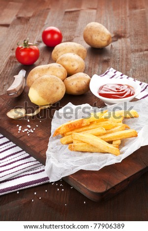 French fries on wooden board with potatoes and tomatoes in background. Country rustical style.