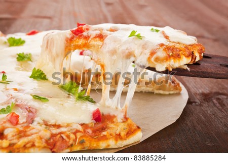 Delicious hot pizza piece on wooden spoon with melting cheese. Rustic pizza concept.