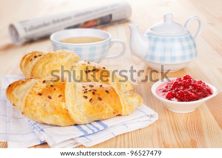 Delicious breakfast. Two croissant, jam, tea and newspaper on wooden background. Sweet french morning concept.