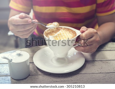 Woman hands with hot cappuccino coffee on a wood table.