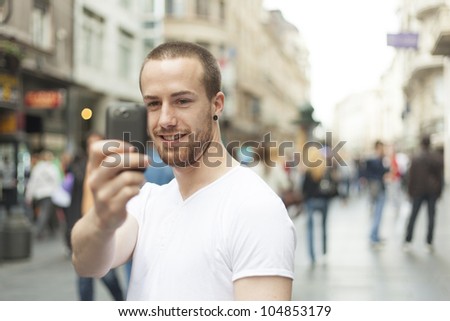 Men on street photographing with mobile phone, background is blured city