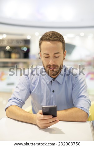 Smiling Businessman with electronic device on hand, blurred background of indoor shopping mall