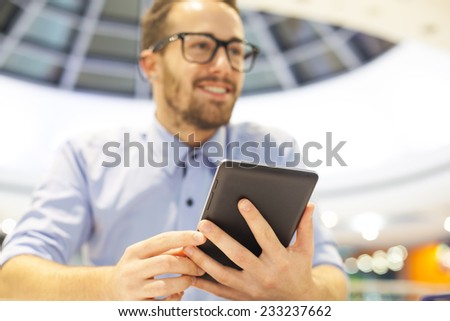 Smiling Businessman with electronic device on hand, blurred background of indor shopping mall