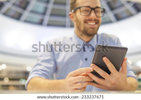 Smiling Businessman with electronic device on hand, blurred background of indor shopping mall