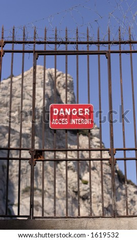 locked gate with danger sign in french and cliffs in background