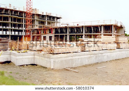 construction site work in progress . lumber and foundation concrete in the foreground with crane and incompleted multi storey levels in the background