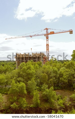 crane and construction building with green space in the foreground and sky