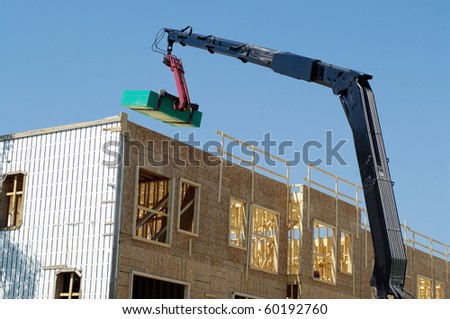 crane lifting pile of wooden planks to the top of building in construction