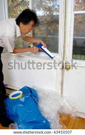 man using caulk gun caulking  window sill to winterize insulate home