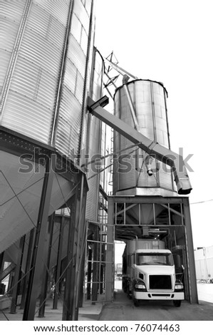 agricultural industry abstract of wheat and grain commercial storage container steel bins with chute and transportation truck . black and white.