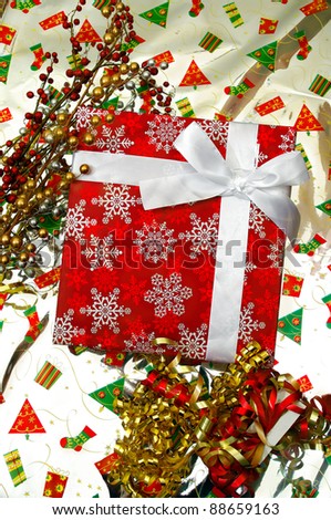 christmas present red box with snow flakes and silk ribbon bow  with seasonal holiday ornaments and shiny wrapping paper