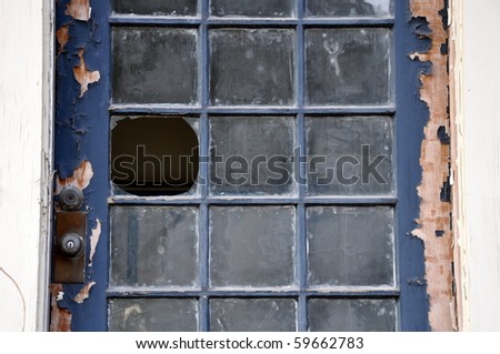 Landscape orientation close up of broken window pane in an old door with peeling paint.