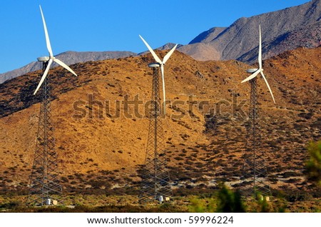 Three power generating windmills against mountains and sky.