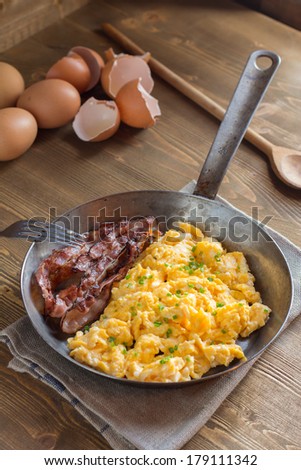 Overhead view of scrambled eggs with bacon in frying pan