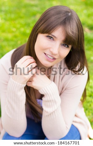 Young woman sitting on grass in pink cardigan sweater
