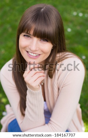 Smiling young woman with hand on chin in pink cardigan sweater