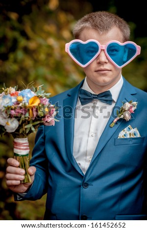 funny  groom outdoor portrait  with multi-colored glasses in the shape of heart