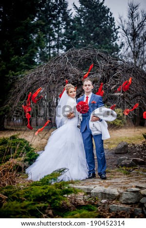 young wedding couple, beautiful bride with groom portrait on outdoor. tree decorated with red hearts. Funny couple